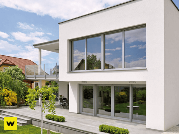 Modernes Einfamilienhaus mit großen Fenstern, Terrasse und Garten bei sonnigem Wetter.
