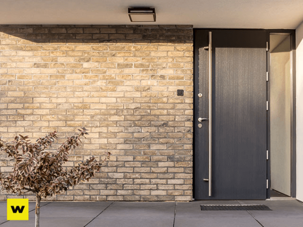 Moderne Haustür aus dunklem Holz vor heller Klinkerfassade mit kleiner Pflanze davor.